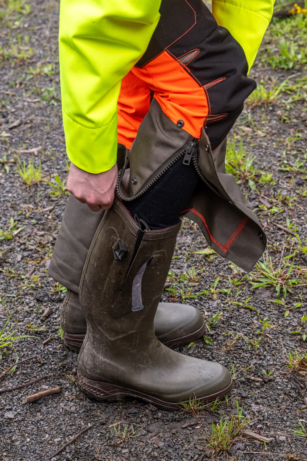 Hand schließt den Reißverschluss der Gamasche der Sau Protect Profi in Orange über dem Gummistiefel